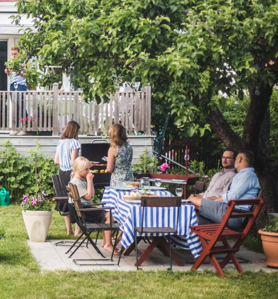 Family getting together around a picnic table and a grill in their backyard