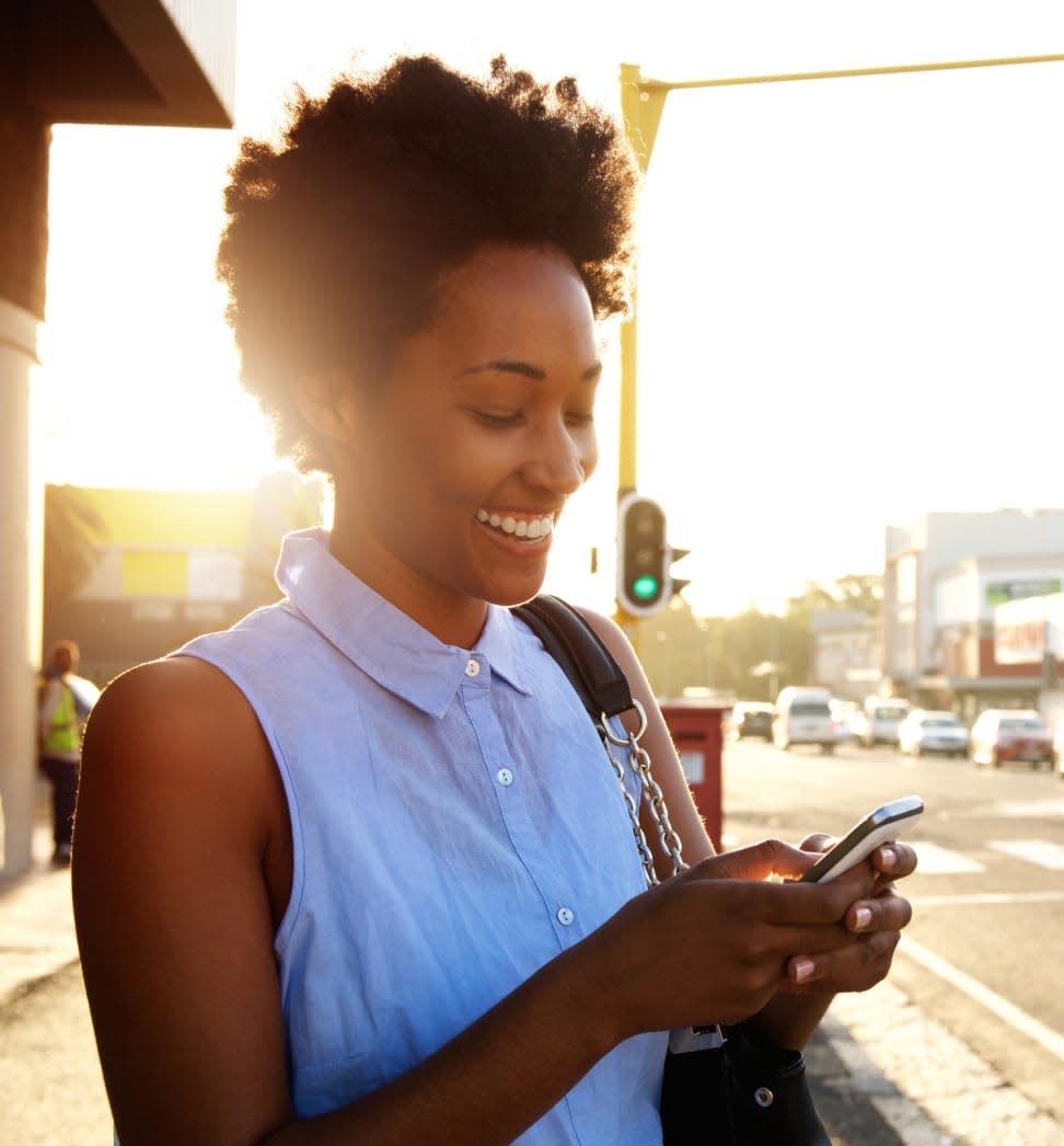 Woman on the sidewalk looking down at her phone smiling